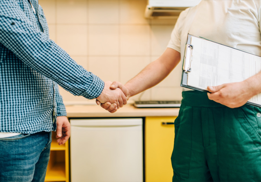 Técnico a apertar a mão a um cliente na cozinha, com uma prancheta na mão